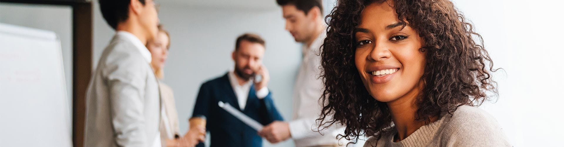  Femme souriante au premier plan et 4 personnes discutant debout lors dune réunion