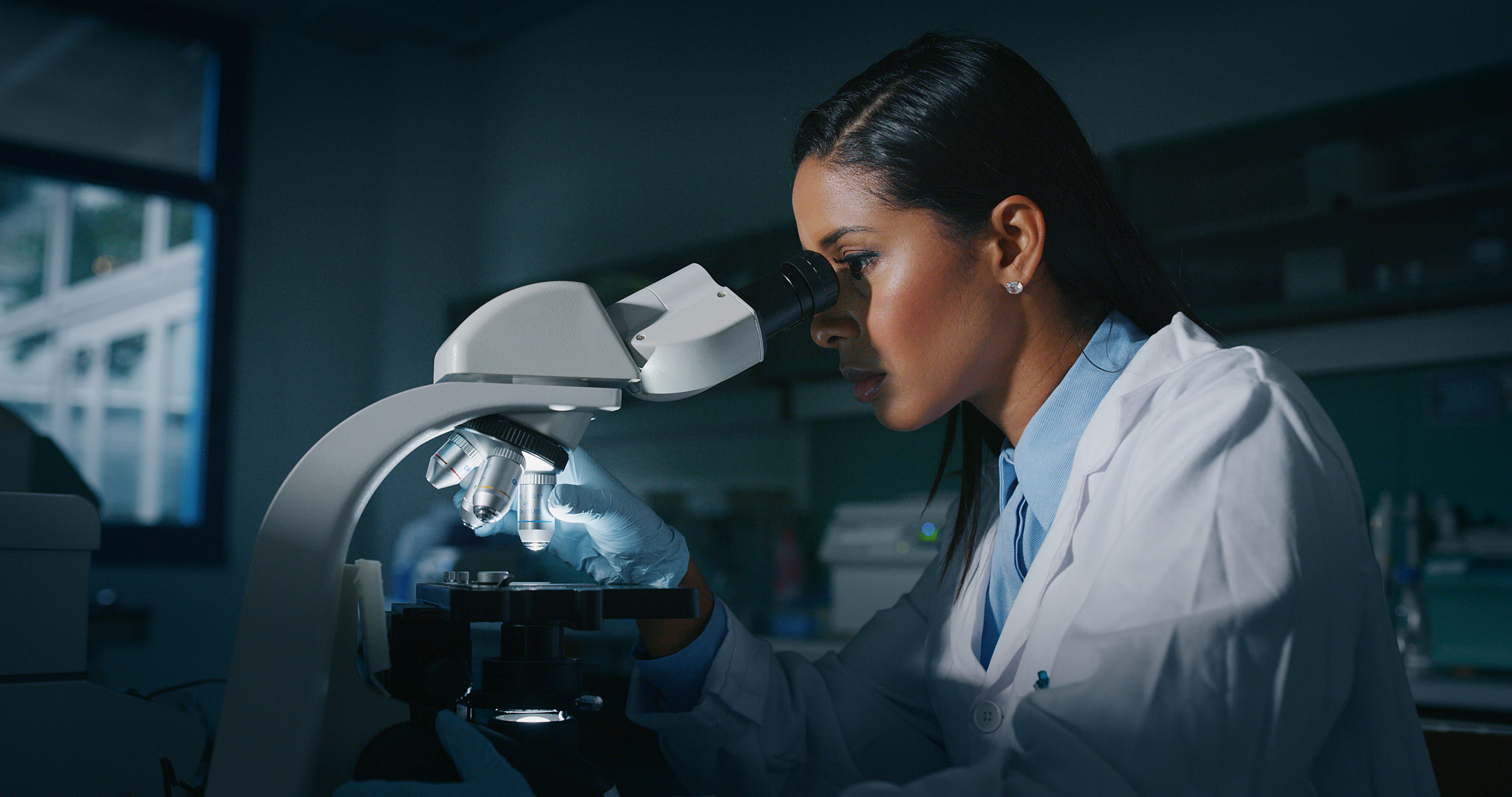 person in lab coat looking into microscope